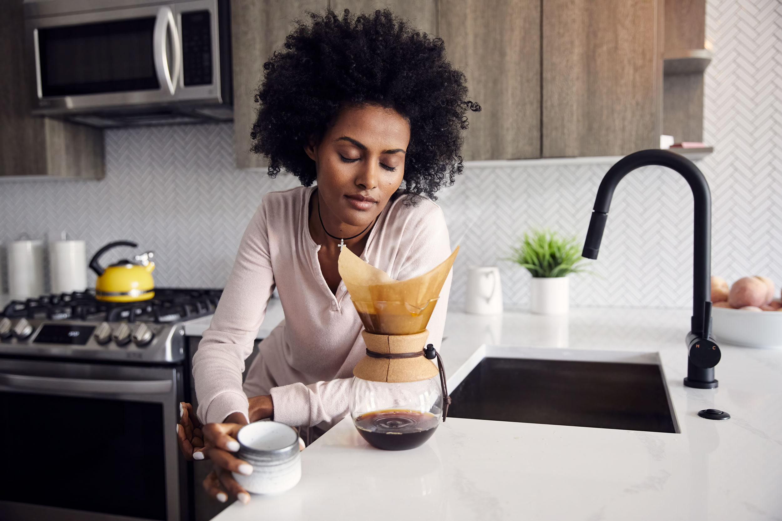 A woman smells freshly brewed pour over coffee in her kitchen.