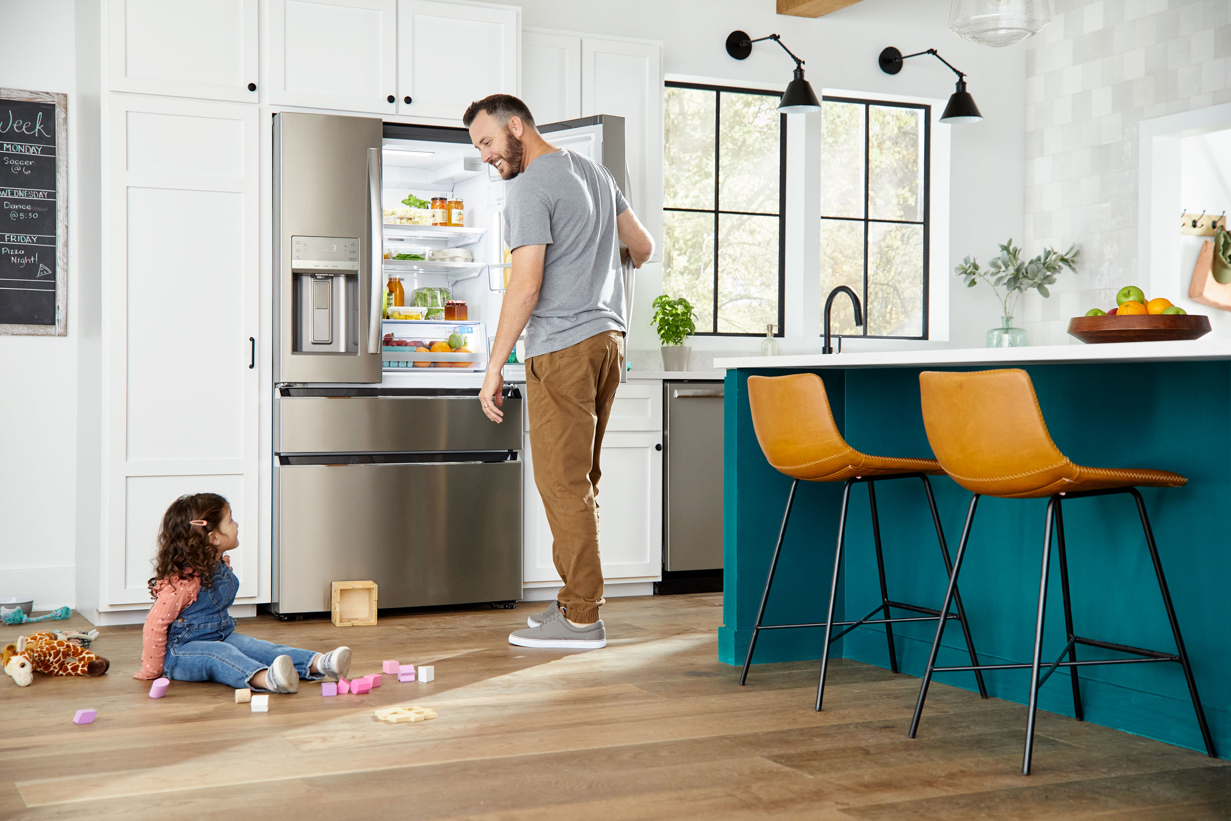 Home lifestyle: A father checks a refrigerator while his young daughter plays on the floor.