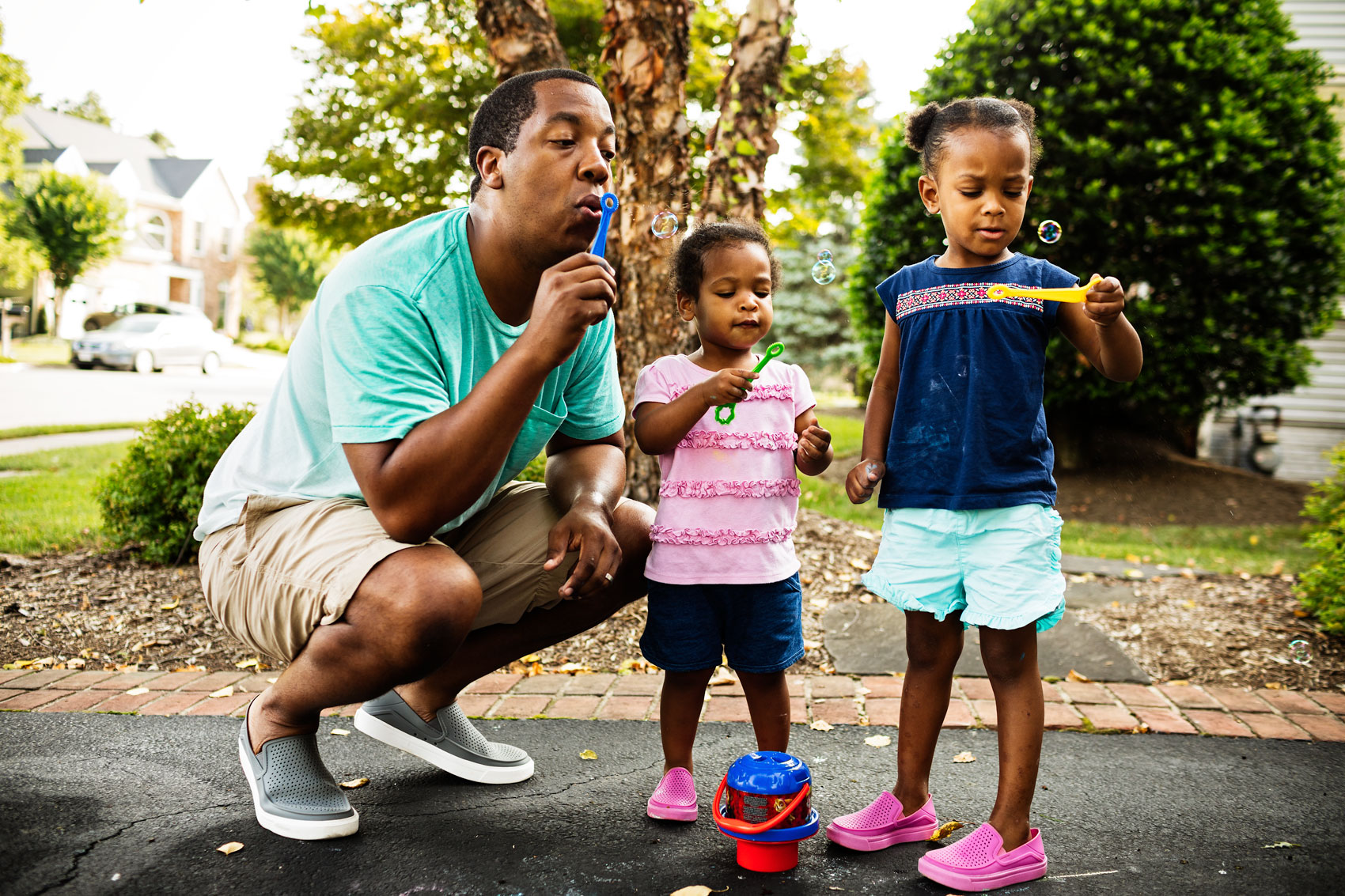 father blowing bubbles with two daughters in driveway, washington dc commercial photography