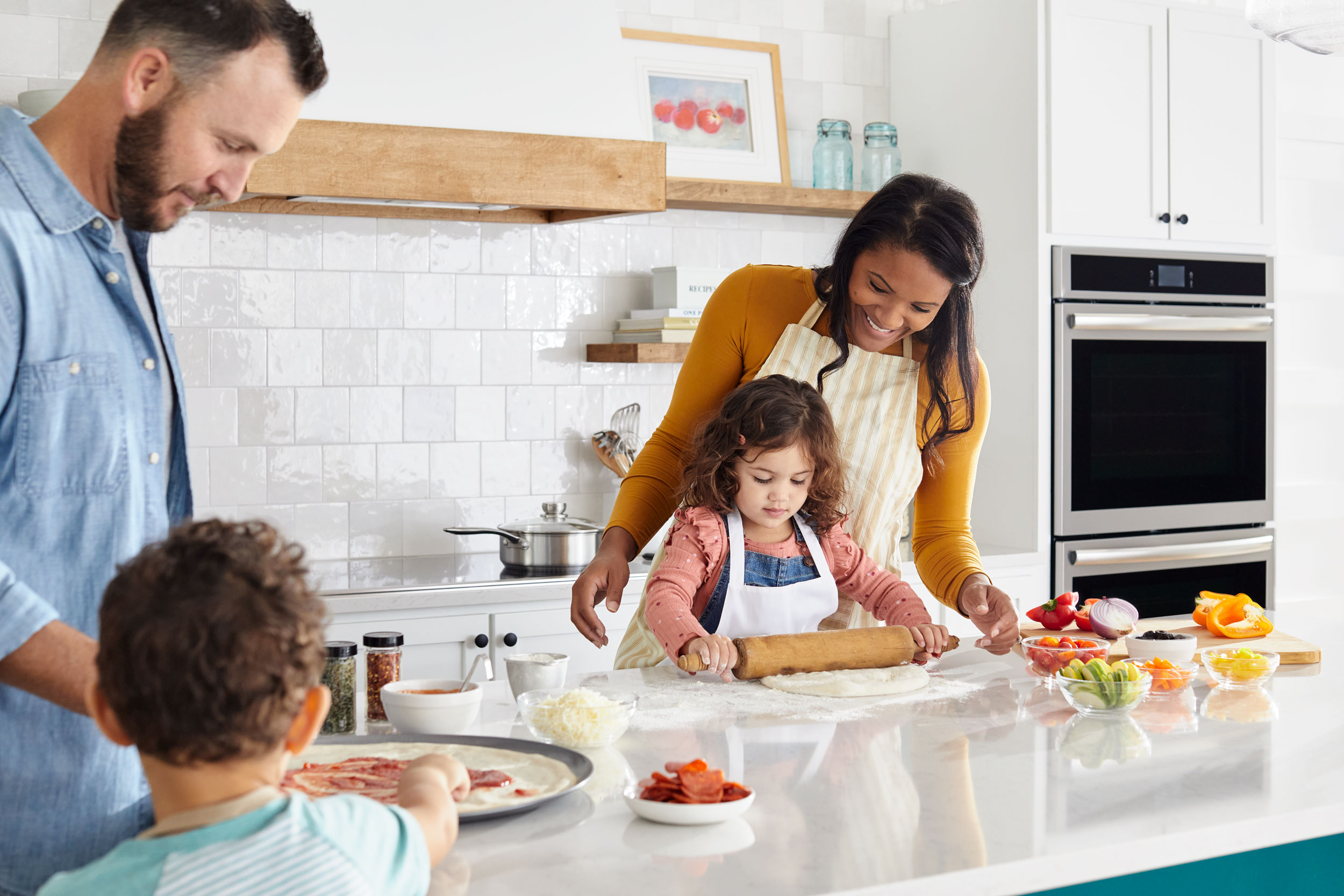 A family makes pizza together in a kitchen.